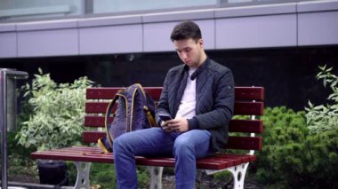 Genç adam kullanma Smartphone sokakta bankta oturmuş. 4 k Video klip