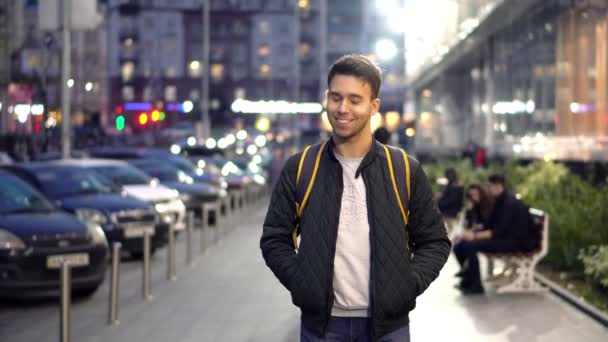 ピンぼけ光効果で夜の通りに立っている若い幸せな笑みを浮かべて男 ビデオ クリップ — ストック動画