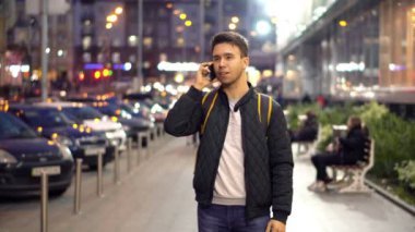 Genç adam konuşarak telefon akşam şehrin bokeh ışık efekti ile sokak. 