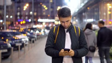 Genç çekici adam kullanma Smartphone akşam şehrin bokeh ışık efekti ile sokak.