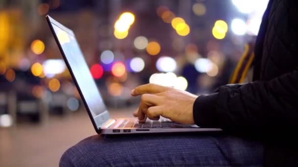 夜の都市の通りピンぼけ光効果でノート パソコンで働いていた男性のクローズ アップ ビュー — ストック動画