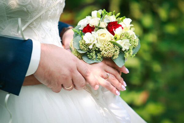 wedding rings on the fingers of the bride and groom on a bridal bouquet