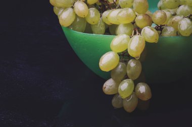 karanlık bir arka plan üzerine bir tabak içinde üzüm demet