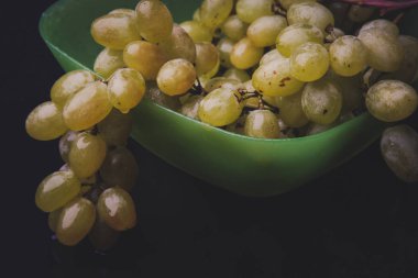 karanlık bir arka plan üzerine bir tabak içinde üzüm demet