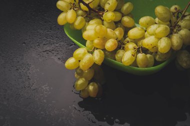 karanlık bir arka plan üzerine bir tabak içinde üzüm demet