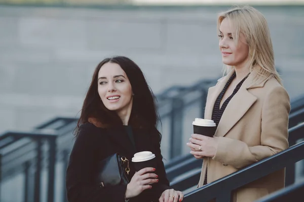 two women walk in the city, drink coffee and enjoy the rest