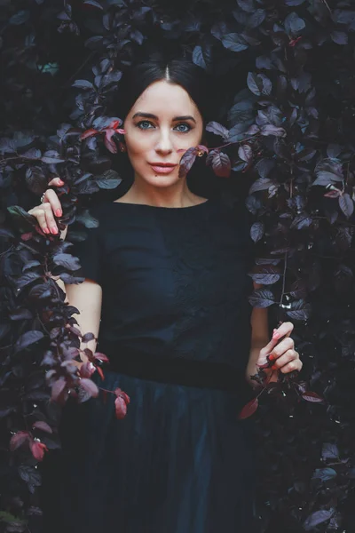 庭の葉に黒いドレスを着た美しい女性 — ストック写真