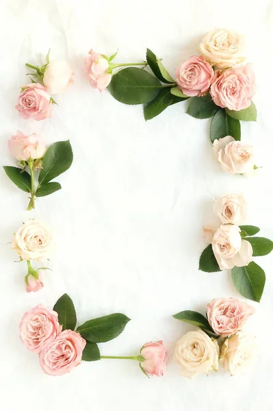 Flowers background. A frame of gently pink and beige roses on white linen fabric. top view. copy space