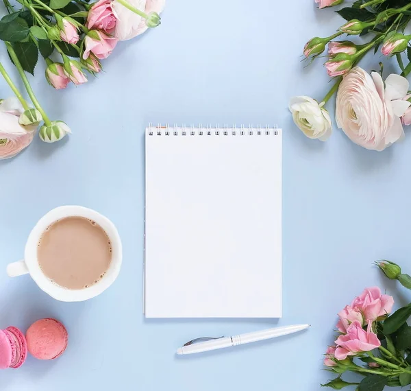 Holiday background. cup of cocoa, macaroons cookies colorful in pastel colors , delicate pink ranunculus flowers and notebook on a pale blue background. Top view. Flat lay. Copy space