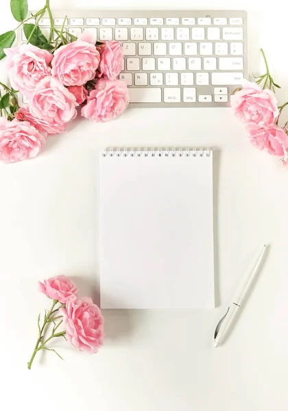 Office feminine desk, female accessories, workspace with laptop, notebook and bouquet beautiful pale pink roses. Holidays concept.Copy space