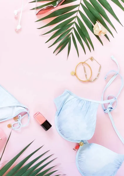 gevşeme, bir mayo, güneş gözlüğü, kadın giyim moda kolaj yapmak aksesuarları ve palmiye yaprakları soluk pembe bir arka plan üzerinde. Düz yatıyordu. üstten görünüm. Kopya alanı