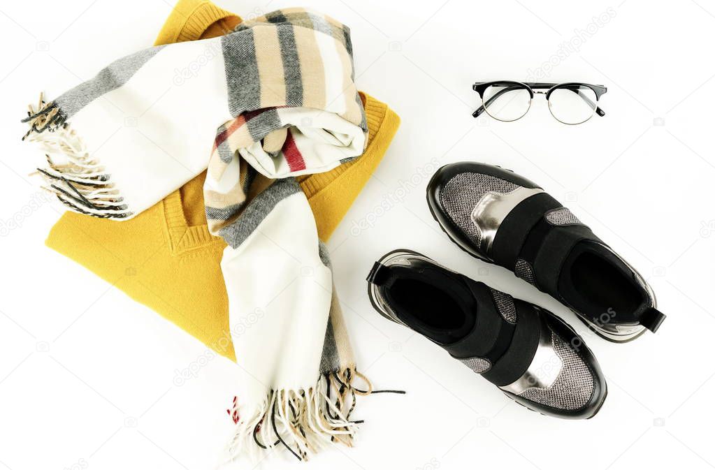 Flat lay, top view woman fashion clothes and accessories set on white background.   modern and casual outfit- sweater, scarf, glasses, sneackers. 