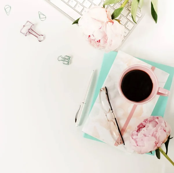 Flat lay women\'s office desk. Female workspace with laptop, flowers peonies, accessories, notebook, glasses, cup of coffee on white background. Top view feminine background.Copy space