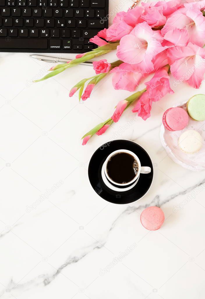 Flat lay women's office desk. Female workspace with laptop,  flowers pink gladioluses ,  accessories, glasses, cup of coffee on marble desk  background. Top view feminine background.Copy space