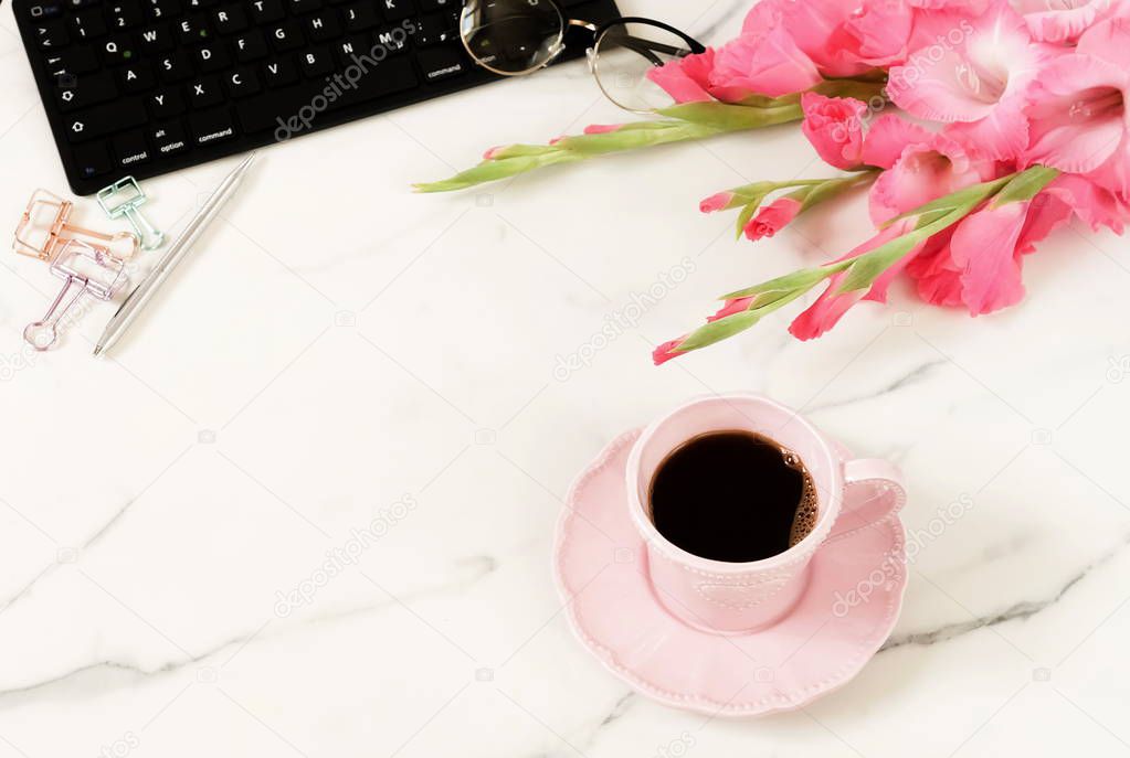 Flat lay women's office desk. Female workspace with laptop,  flowers pink gladioluses ,  accessories, glasses, cup of coffee on marble desk  background. Top view feminine background.Copy space