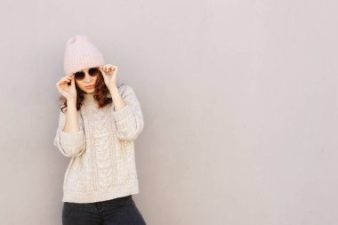 genç çekici uzun saçlı hippi kız bir kazak, kot pantolon, spor ayakkabı ve şapka duvarın yanında. kopya alanı