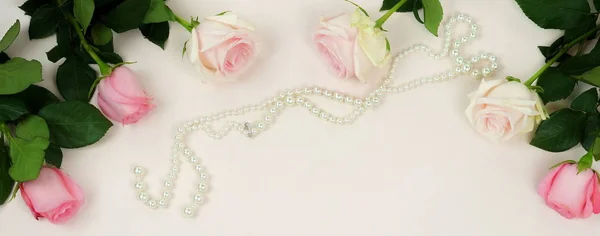 Banner from Bouquet of beautiful pink roses and pearl jewelery on  pale pink background.Top view.Copy space
