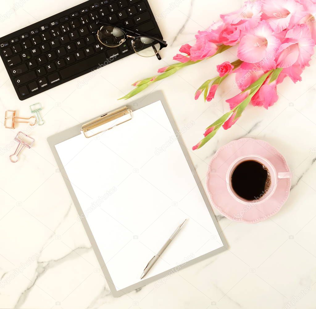 Flat lay, top view women's office desk with  flowers. Holiday workspace with laptop, clipboard,  pink gladioluses ,accessories, glasses, cup of coffee on marble desk  background.  Copy space
