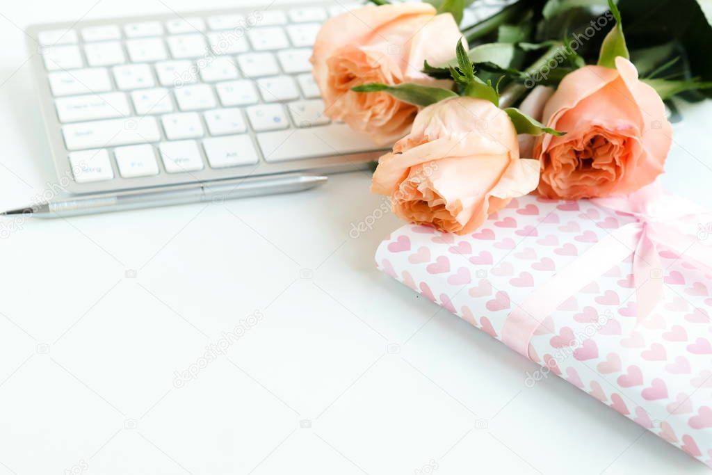 Valentine's day background. Women's office desk, female workspace with keyboard,  flowers roses living coral color,  gift, accessories on white background. Copy space. 
