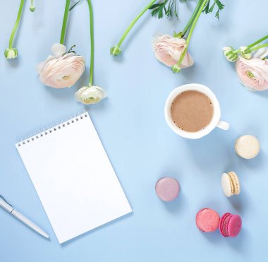 boş defter, fincan kahve, macarons ve tipik çiçekler mavi zemin üzerine Üstten Görünüm