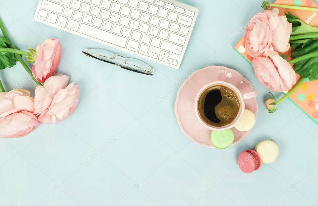 female workspace with keyboard, ranunculus flowers and cup of coffee on blue background 
