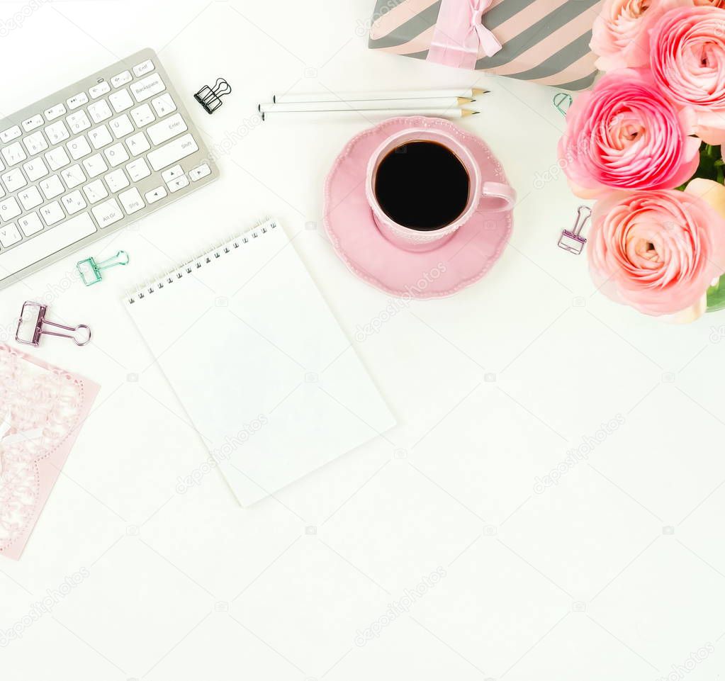 female workspace with keyboard, ranunculus flowers and pink cup of coffee