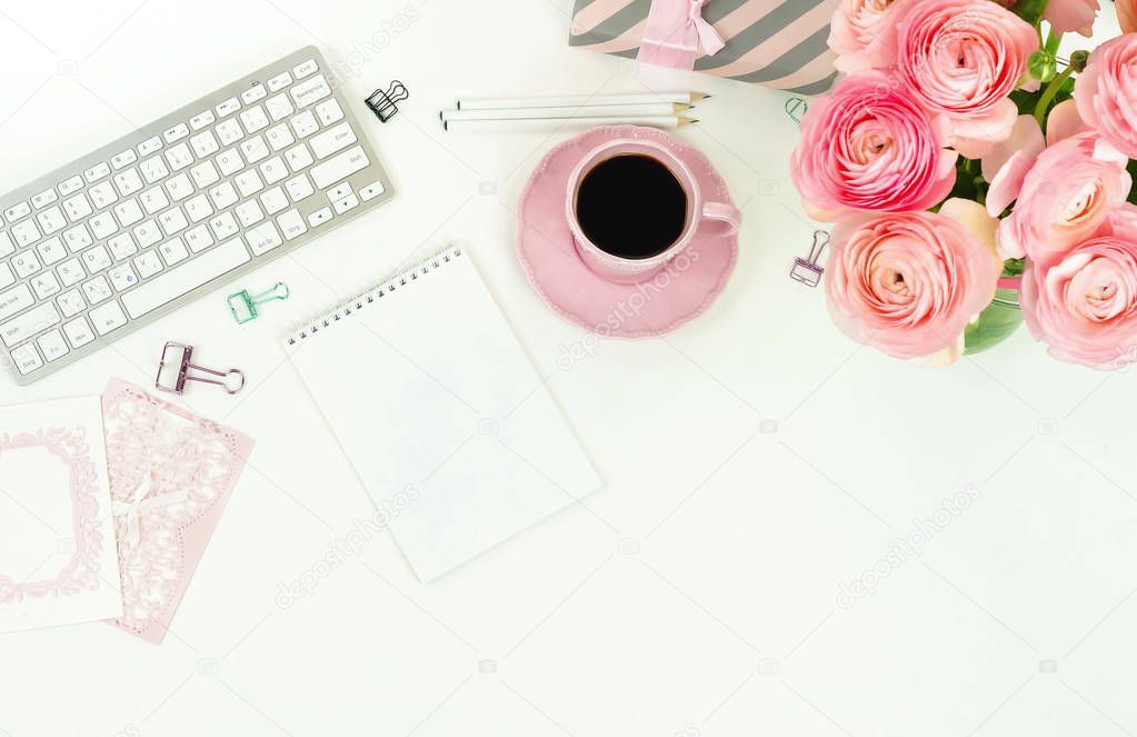 female workspace with keyboard, ranunculus flowers and pink cup of coffee