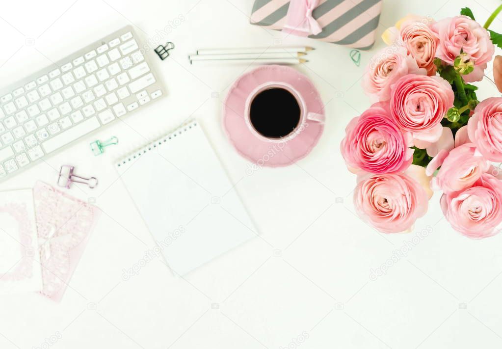 female workspace with keyboard, ranunculus flowers and pink cup of coffee