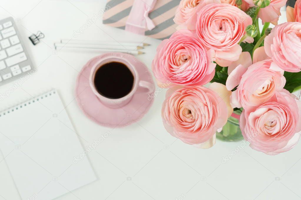 female workspace with keyboard, ranunculus flowers and pink cup of coffee
