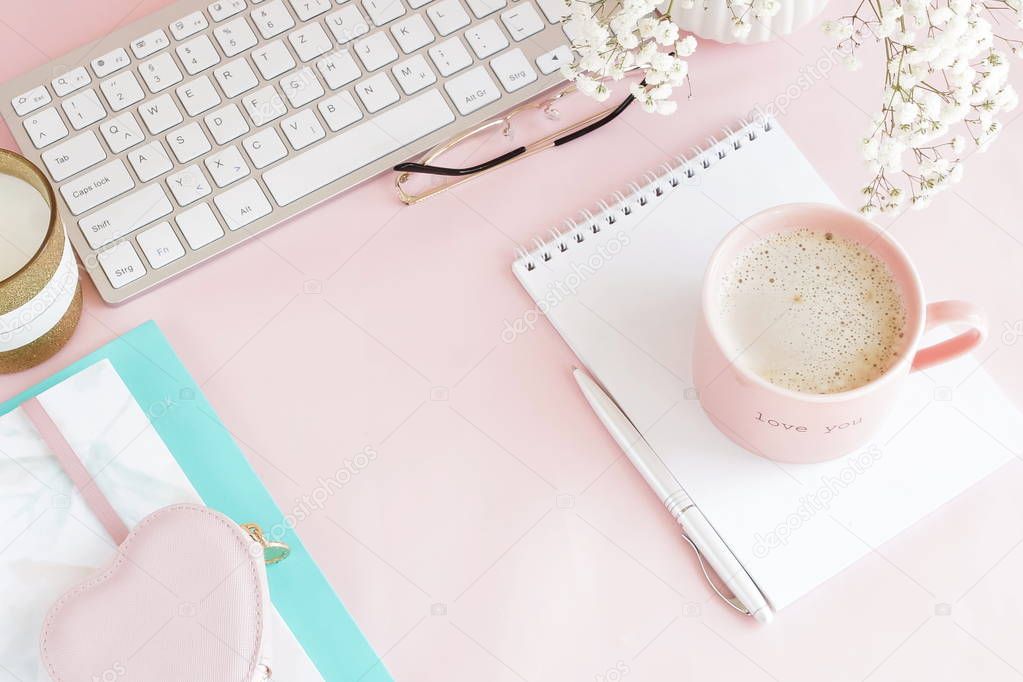 female workspace with keyboard and cup of coffee on pink background 