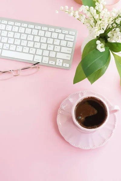 cup of aromatic coffee at pink workplace with keyboard and flowers