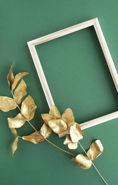 Golden eucalyptus leaves and golden frame mock up om green background top view, flat lay, copy space. Greetings floral minimal card