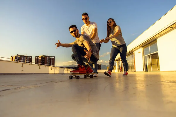 Dva Kavkazští Přátelé Tlačí Svého Přítele Skateboardu Střeše Budovy — Stock fotografie