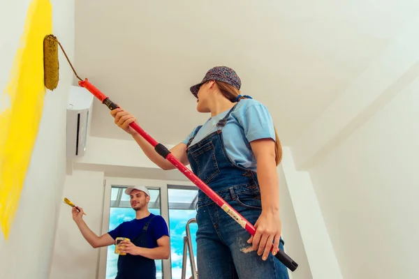 Chica Pintando Pared Con Pintura Amarilla Mientras Novio Sostiene Pincel —  Fotos de Stock