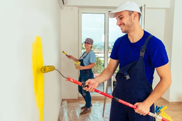 Young couple painting wall at home in yellow with paintbrush and paint stick roller