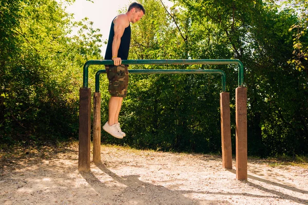 在森林体育馆的金属棒上做俯卧撑的运动男人 — 图库照片