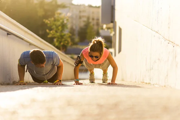 都市場所の地面に腕立て伏せをやってスポーツウェアのカップル — ストック写真