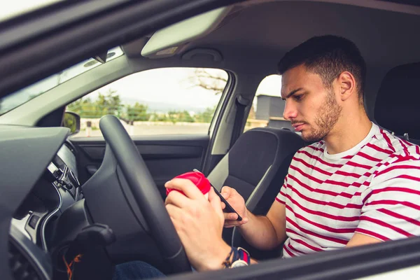 A guy in car is holding coffee in one hand and looking in his phone while driving risky