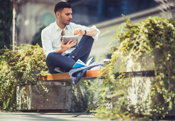 stock image A man is looking amazed at his white tablet while is sitting outside on bench