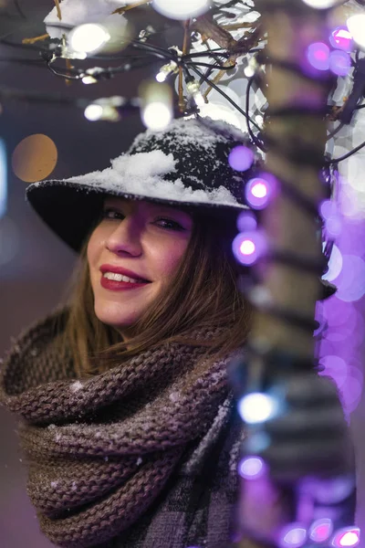 下がり 雪が降って雪の夜クリスマス ツリーのライトの前に立って雪と黒い帽子の少女 — ストック写真