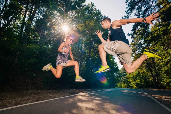 公園の近くの道路でジャンプしながら屈託のないカップルを楽しませる — ストック写真