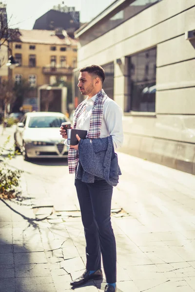 都市のビジネスマンがコーヒーを飲みながら彼の正面を見ている美しい街に立っています — ストック写真