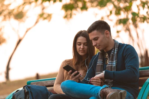 Casal Jovem Ouvindo Música Sorrindo Olhando Para Telefone Sentado Banco — Fotografia de Stock