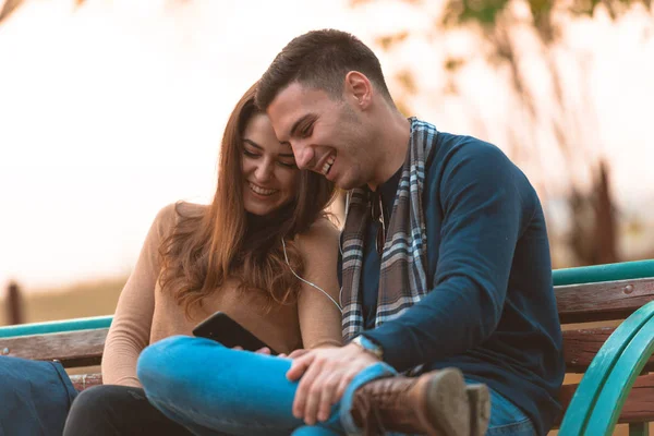 Casal Jovem Ouvindo Música Sorrindo Olhando Para Telefone Sentado Banco — Fotografia de Stock