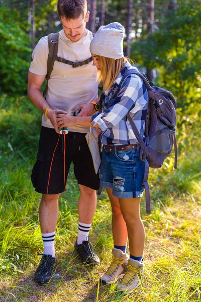 森の中を歩いている間に若いカップルが音楽をチェックする 夏の山の中のハイキングのコンセプト — ストック写真