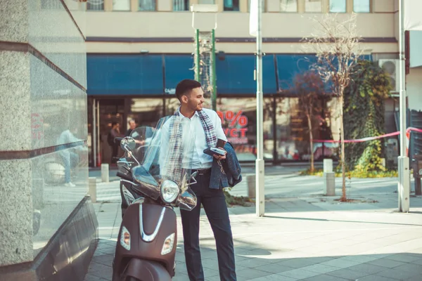 一位穿着白衬衫 穿着灰色外套的自信的年轻商人站着 穿着停在城市广场的摩托车看着 — 图库照片