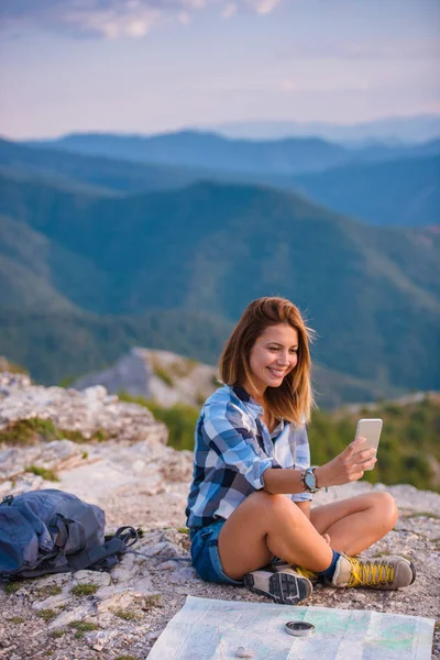 夕暮れ時に山の頂上から携帯電話で自撮りしている女性 — ストック写真