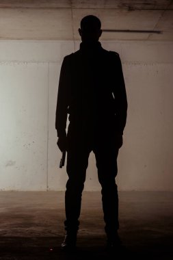 Silhouette of a man standing still with a revolver in his hands clipart