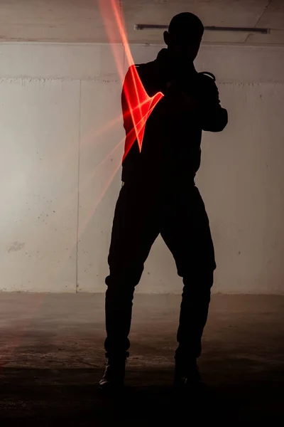 Silhouette of a male person who is standing in dark room and holding gun with laser
