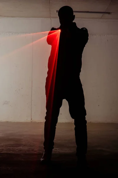 Silhouette of a male person who is standing in dark room and holding gun with laser